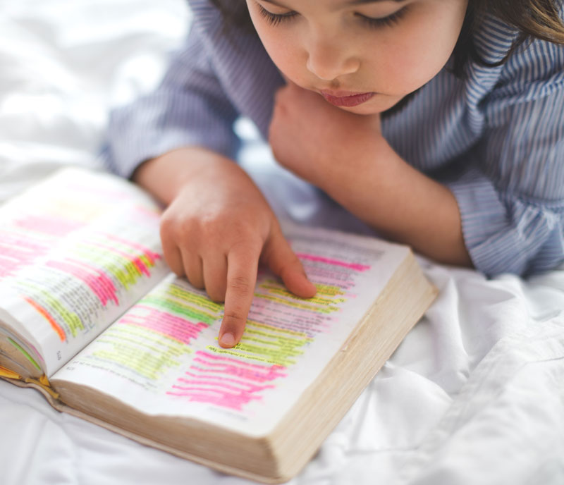 Little Girl Reading From Bible While Lying In Bed Cropped