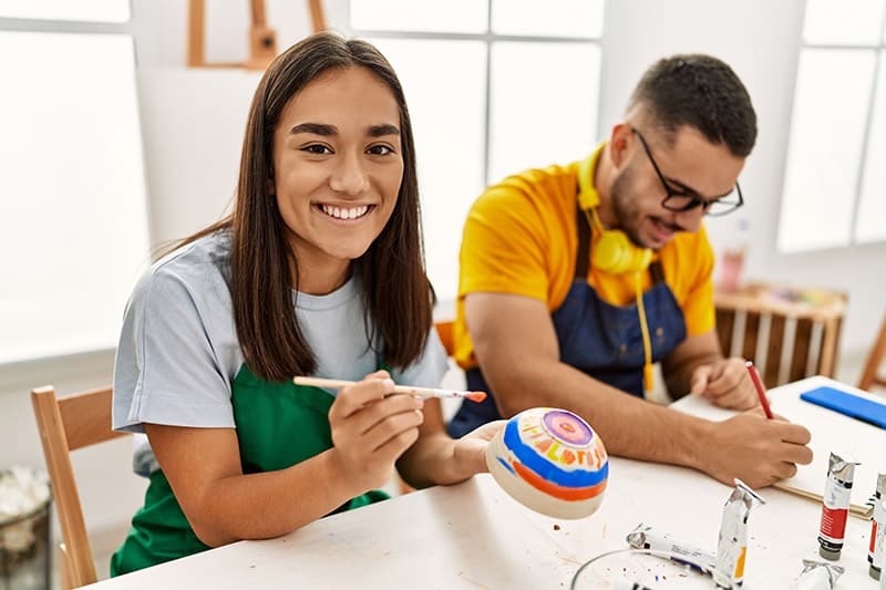 Young Hispanic Couple Smiling Happy Drawing Sitting On The Table At Art Studio.