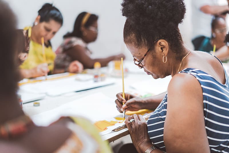 Group Of Brazilian Women Painting Textiles In Work Room Of Social Project