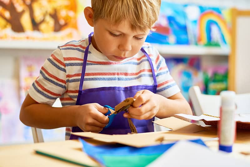 Little Boy Cutting Paper In Craft Class