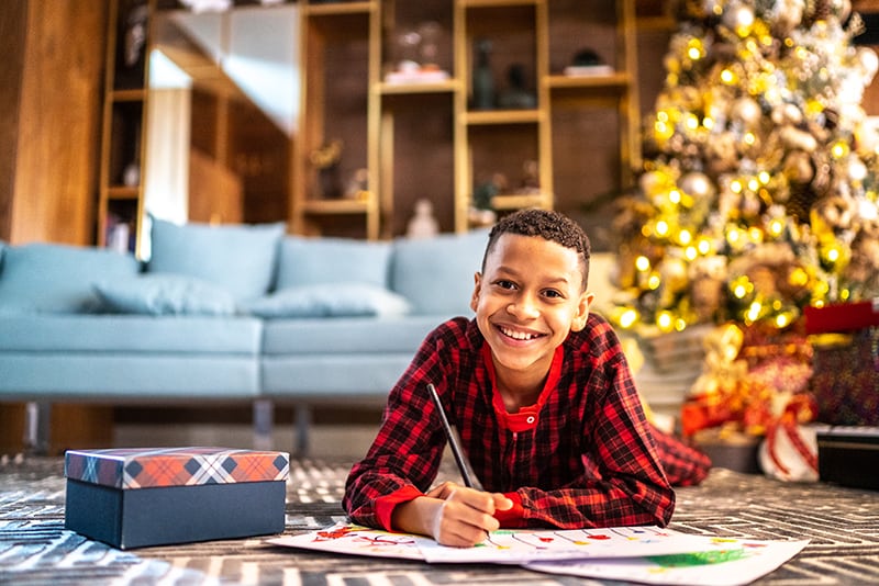 Portrait Of A Happy Boy Lying On The Floor Coloring a Picture During Christmas