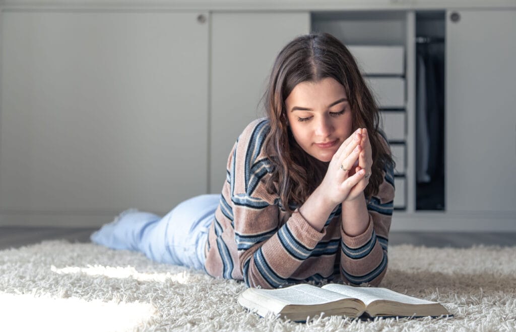 A Young Woman Is Reading The Bible While Lying On The Floor.